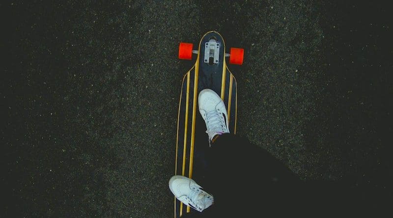 Zwei Beine und weiße Turnschuhe auf Skateboard