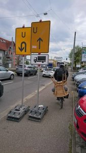 Radfahrer mit Stuhl auf Gepäckträger umkurvt Umleitungsschilder