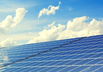 Mit Solarzellen belegtes Hausdach vor bewölktem blauem Himmel