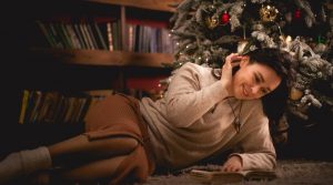 Junge Frau liegt vorm Weihnachtsbaum und liest ein Buch