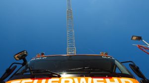 Blick von der Front eines Feuerwehrfahrzeugs die Drehleiter hinauf zum blauen Himmel