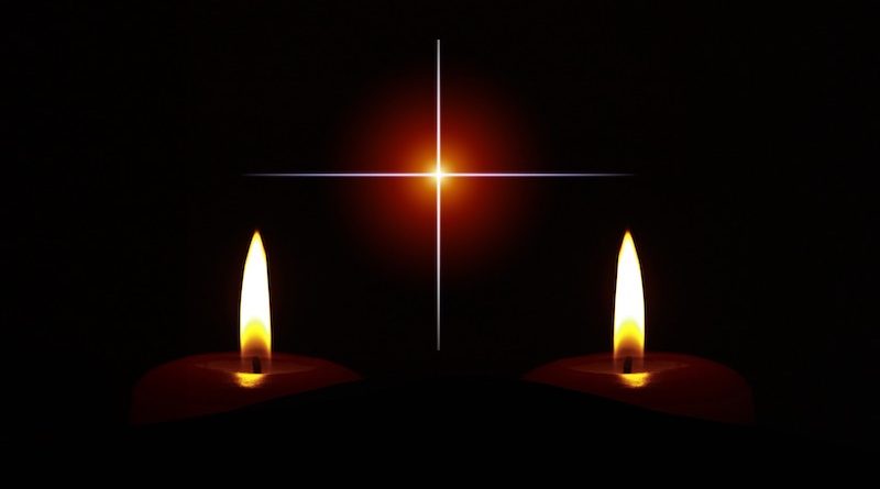 Zwei brennende Kerzen vor einem Kreuz