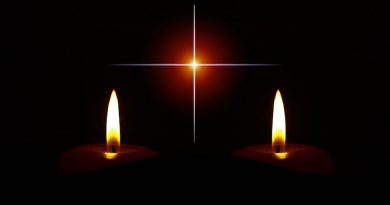 Zwei brennende Kerzen vor einem Kreuz