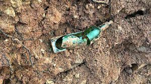 Zerbrochene grüne Flasche im Erdreich hinter einer entfernten Weinbergmauer