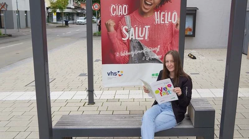 Junge Frau sitzt mit VHS-Heft in der Hand an einer