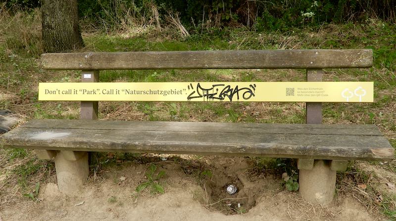 Sitzbank im Eichenhain mit verschmiertem Infoschild