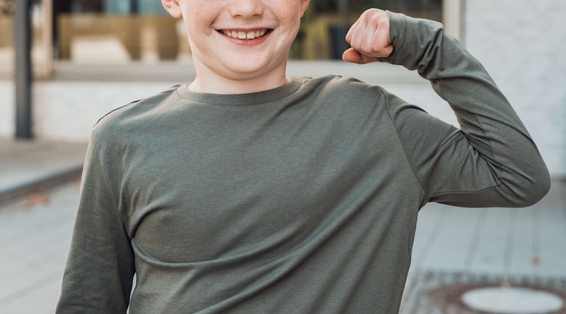 Junge zeigt Muskeln des linken Arms