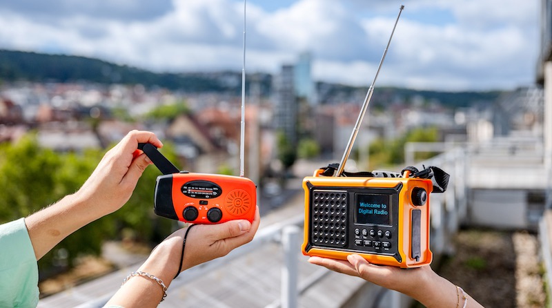 Zwei Notfallradios in Händen gehalten, dahinter die Innenstadt von Stuttgart