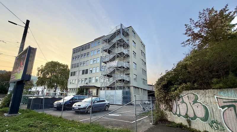 Wohnheim an der Inselstraße 33 hinter Maschendrahtzaun und parkenden Autos